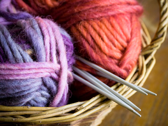 wicker basket with knitting needles and balls of yarn